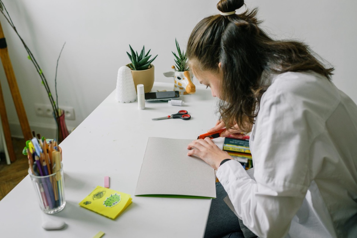 A student at a desk cutting printed flashcards from a sheet of paper with scissors